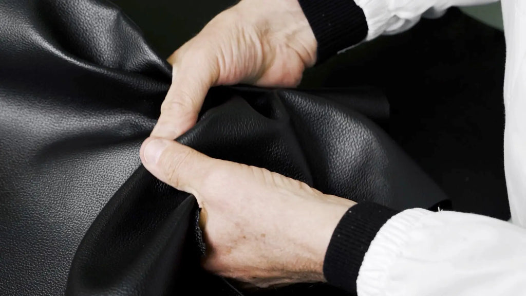 Close-up of a craftsman's hands in white gloves demonstrating the flexible quality of Trevony's black lambskin leather, indicative of the brand's high standards for material selection and durability.