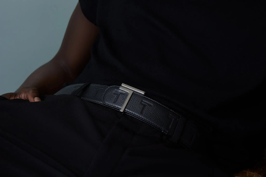 A dimly lit image of a person wearing a dark outfit with the Trevony Truth belt, featuring a leather strap and a distinctive silver buckle.