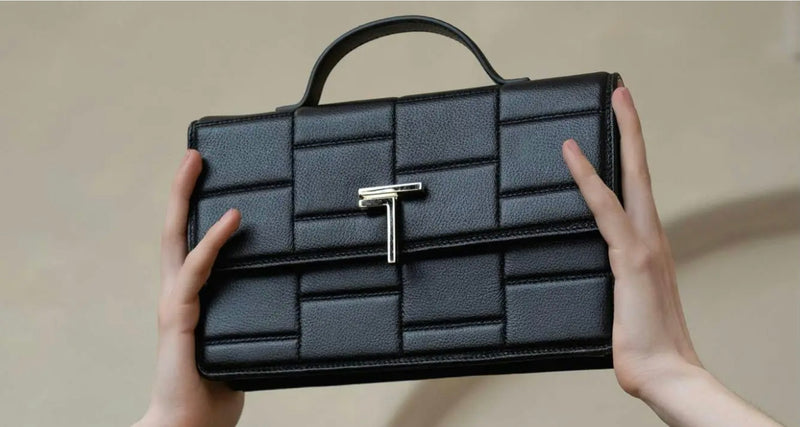 Black medium Minerva handbag with a gold clasp held by hands against a neutral background